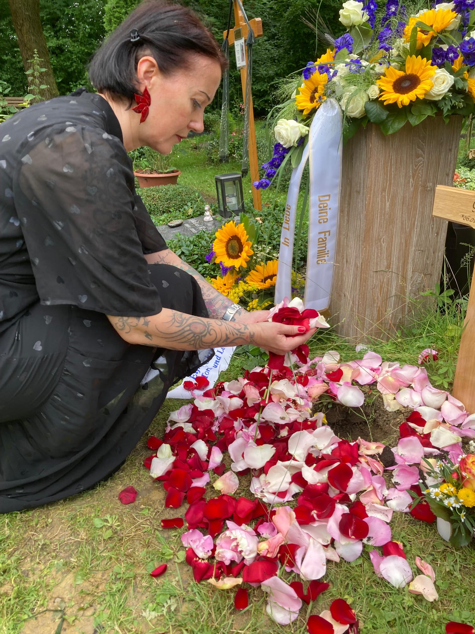 Judith Brauneis streut Rosenblätter auf ein Grab mit Blumen und Sonnenblumen
